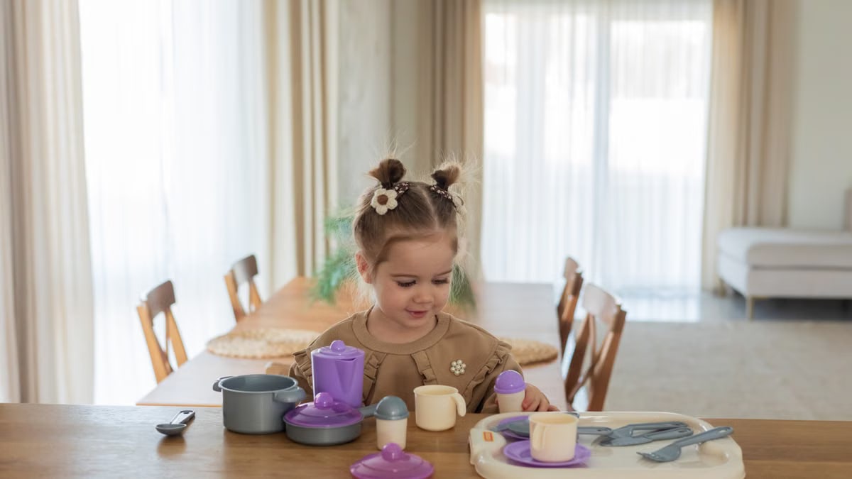 Young girl enjoying playtime with toy dishes on a sunny day indoors.